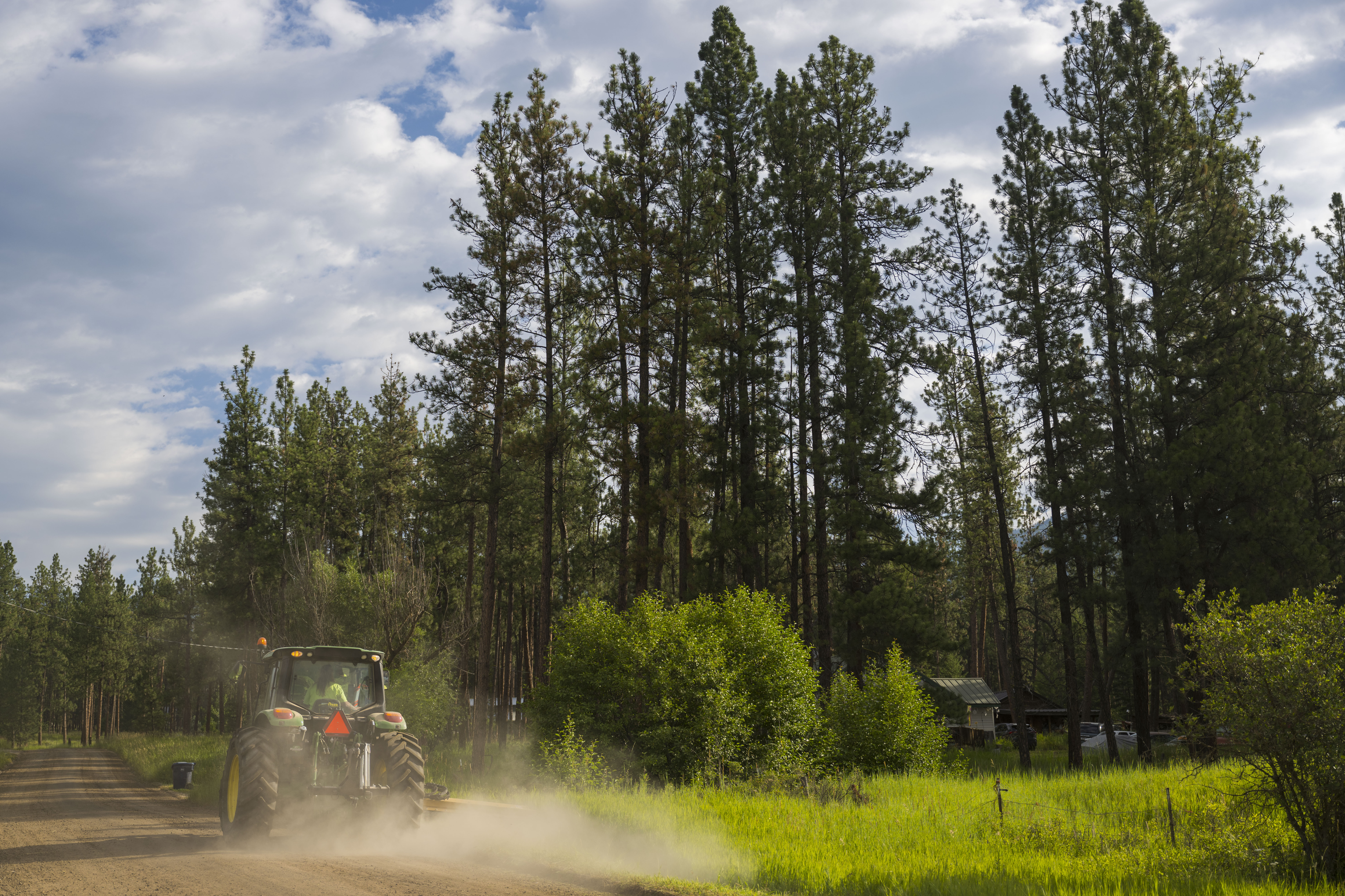 Tractor on a gravel road with trees in the background, dust is visible